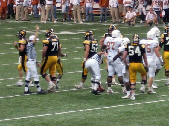 Football players in black and yellow uniforms and white uniforms with referees on a green field