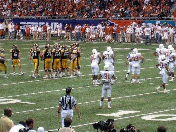 American football game with players in white and black uniforms on the field, spectators in the stands