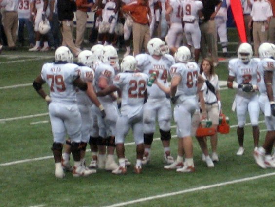 Football players in white uniforms with orange numbers on a field