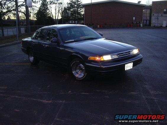 Dark blue Ford Crown Victoria parked in a lot, front quarter view. Has chrome wheels and a license plate