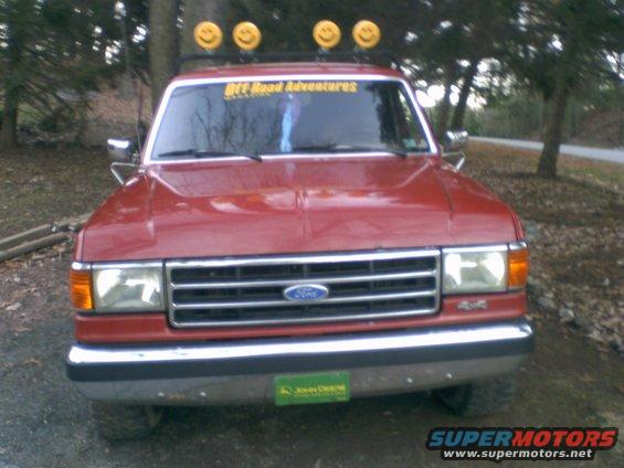 Red Ford pickup truck with smiley face lights on roof rack and 'Off Road Adventures' sticker on windshield