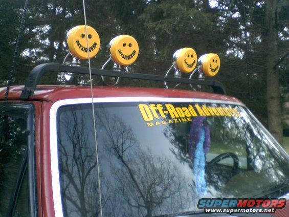 Red SUV roof rack with four yellow smiley face lights and "Off-Road Adventure" magazine sticker on windshield