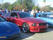 1985 Ford Mustang - A red Saleen Mustang is parked at a car show with other vehicles and people around.