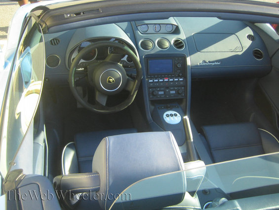 Interior of a Lamborghini with blue seats and dashboard. Steering wheel has a gold emblem