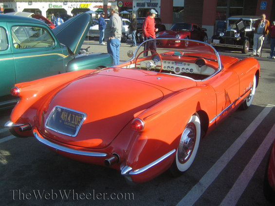 Rear view of red 1955 Chevrolet Corvette convertible with California license plate 4H4105. Green car with hood open in background