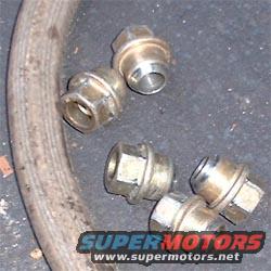 Five lug nuts and a section of rubber hose on a dark surface. Supermotors.net logo visible