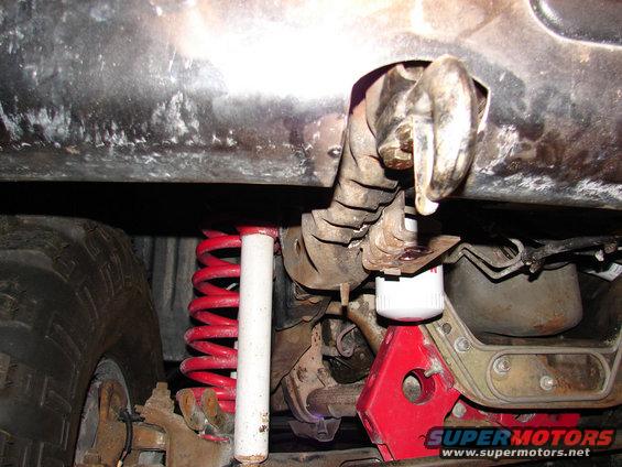 Underside of a vehicle showing a tow hook, red coil spring, shock absorber, and oil filter supported by a red jack stand