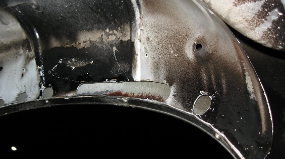 Close-up of a vehicle's inner wheel well showing rust and repair work with visible welds