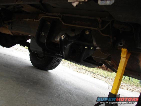 Underside of a vehicle showing a lift kit installed on the rear axle, with a yellow jack stand supporting it
