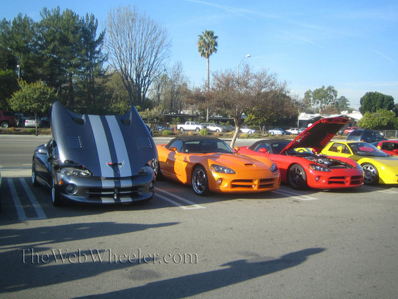 Gray Dodge Viper with hood open and silver stripes, parked next to orange and red sports cars