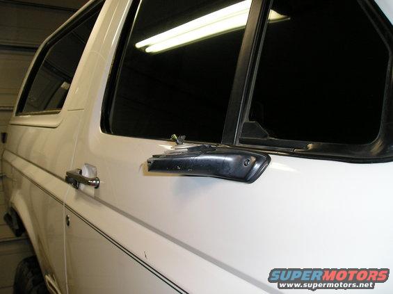 Side view of a white SUV, possibly a Ford Bronco, showing the door handle and window trim. A Supermotors.net watermark is visible