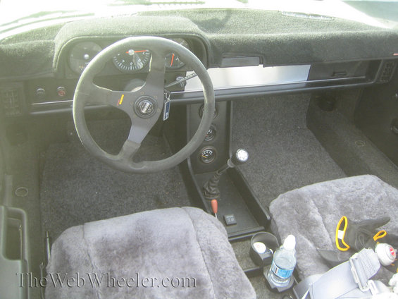 Car interior with sheepskin seat covers, aftermarket steering wheel, and floor shifter
