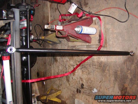 black metal rod with ball joint ends, red straps, jack stands, and spray can on wooden floor