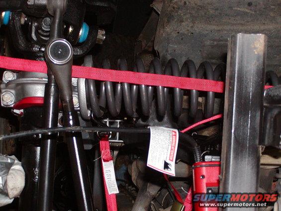close-up of vehicle suspension with red straps around coil spring
