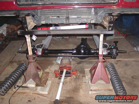 Vehicle front axle assembly supported by jack stands, with springs and a floor jack nearby