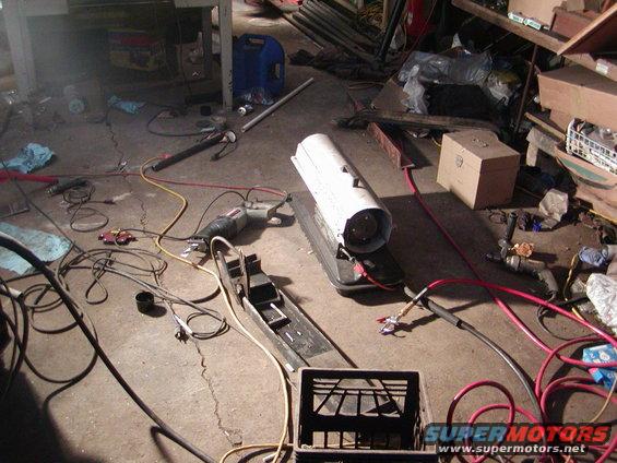 Garage floor with heater, drill, cords, and a crate