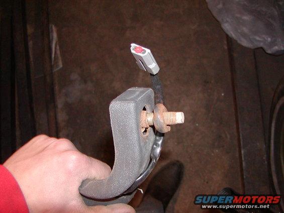 Gray plastic seatbelt buckle with exposed wiring and a rusty bolt, held by a hand in a red sleeve