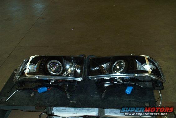 Pair of black projector headlights with chrome accents and blue wiring connectors