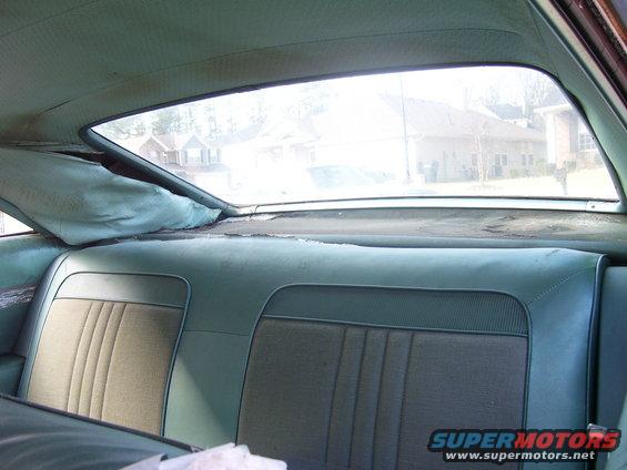 Back seat and rear window of a car, showing worn upholstery and a view of houses outside