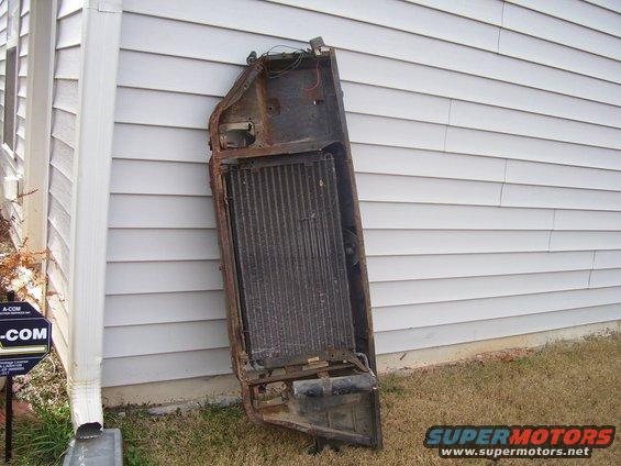 Old car radiator assembly leaning against a house wall