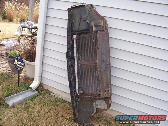 Radiator and grille assembly leaning against a white vinyl-sided wall