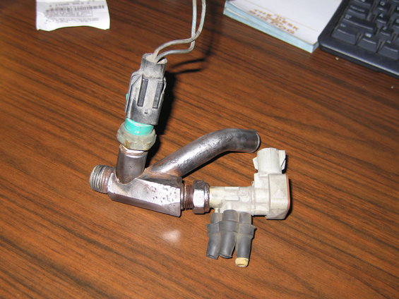 Automotive fuel injector rail with two electrical connectors and four rubber fuel line attachments on a wooden surface