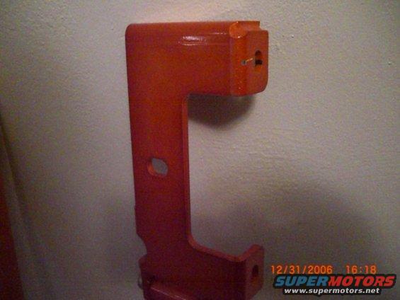 Orange metal bracket with two holes, mounted on a textured wall