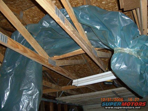 Attic with blue plastic sheeting covering insulation and wooden beams