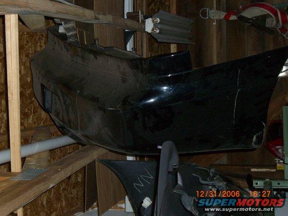 Black car bumper mounted on wooden shelves, with visible damage and a timestamp overlay