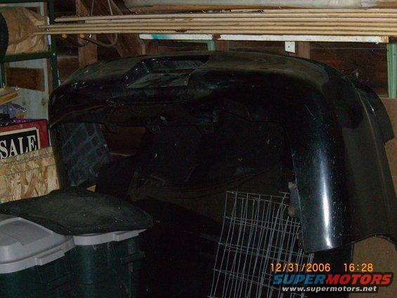 Black car bumper stored indoors, with a 'SALE' sign visible in the background