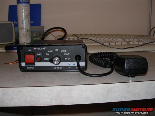 Whelen siren control box with red power button, function knob, and microphone. Text includes 'POWER', 'FUNCTION', 'ON', 'MAN', 'PA', 'RAD', 'HF', 'WAIL', 'YELP', 'PIER'