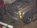 2000 Chevrolet Tahoe - The front bumper of a silver SUV is shown, with the hood open and engine exposed. Tools are scattered around the vehicle.