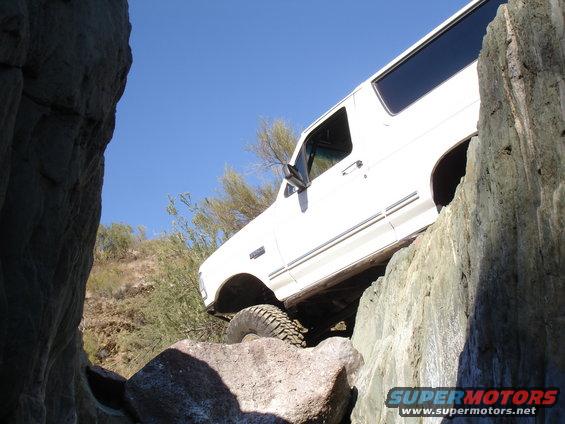 White SUV climbing over large rocks on a trail. The vehicle appears to be a 1992 Ford Bronco