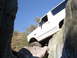 1984 Ford Bronco - A white SUV navigates a rocky obstacle course under a clear blue sky.