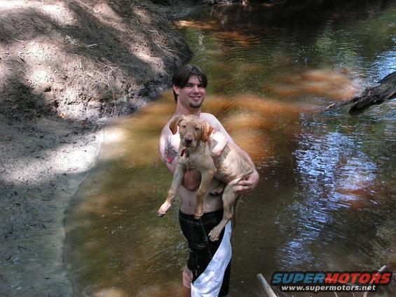 Man holding a dog in a stream with Supermotors.net logo