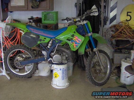 Green and blue 1991 Kawasaki KX250-K2 dirt bike with pink and yellow graphics, parked in a garage