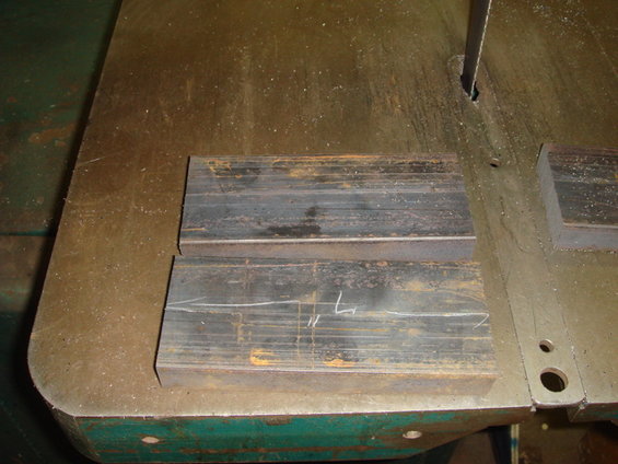 Two metal bars with white markings sit on a workbench next to a band saw