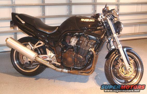 Black Suzuki motorcycle with chrome exhaust and gold brake rotors parked indoors