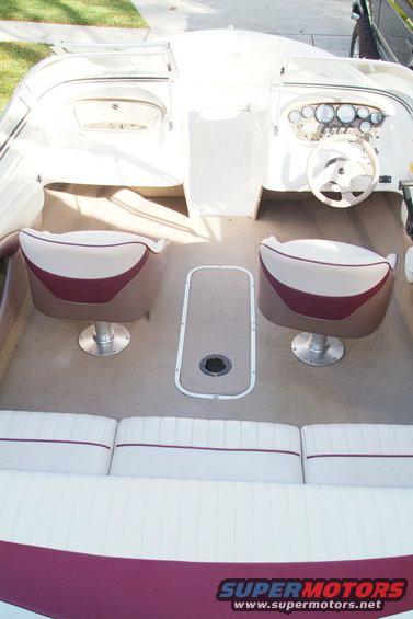 Boat interior with beige and maroon seats, steering wheel, and dashboard gauges