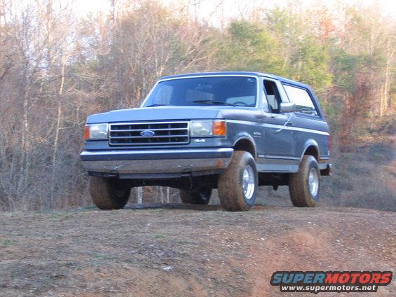 Blue Ford Bronco parked on a dirt hill with trees in the background