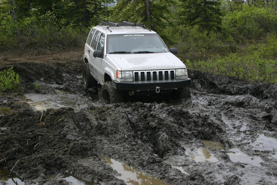 White Jeep Grand Cherokee struggling through a muddy trail with trees in the background