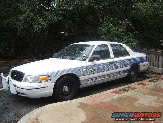 White police car, side view, with 'WEST LAKE HILLS POLICE' text. Appears to be a 1998 Ford Crown Victoria