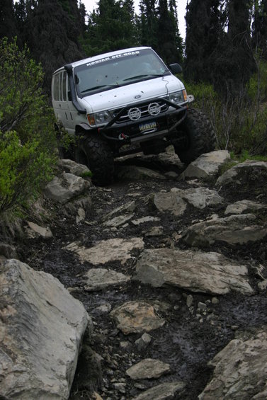 White van with off-road tires navigating a rocky trail