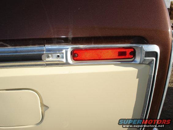 Close-up of a brown and tan vehicle's rear corner, showing a red reflector and chrome trim