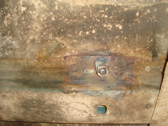 Close-up of rusted metal frame with a bolt and washer securing a bracket. A small circular hole is visible below the bracket