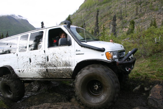 White van with large tires and snorkel driving through mud