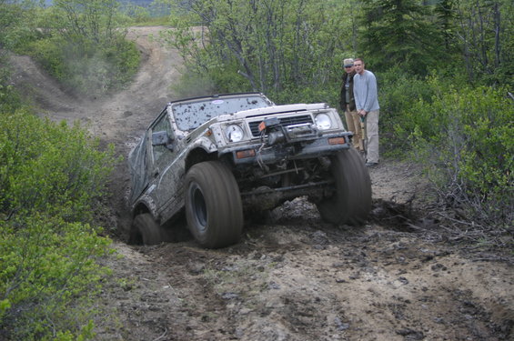 Mud-covered Suzuki Samurai navigating a steep, muddy trail