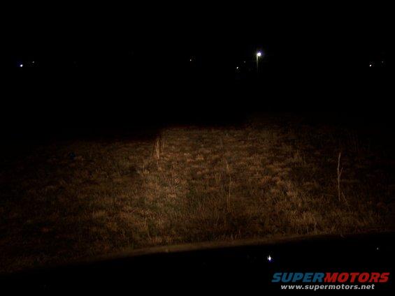 Headlight beam illuminates dry grass at night. Supermotors.net logo visible