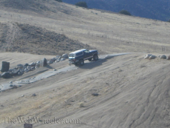 Blue SUV with a white top driving on a dirt road in a dry, hilly landscape