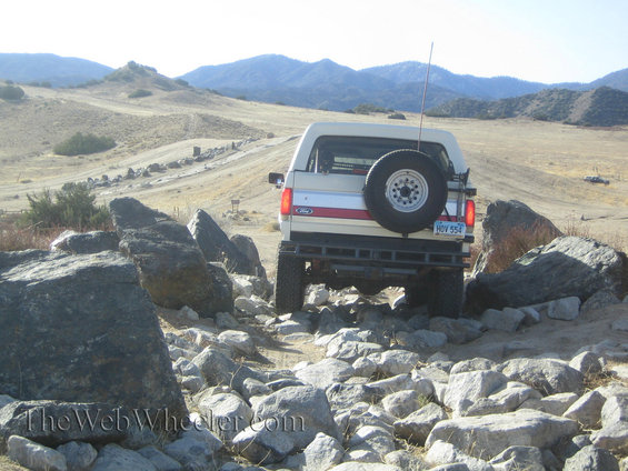 White Ford Bronco II with red stripe, spare tire on rear, navigating rocky terrain
